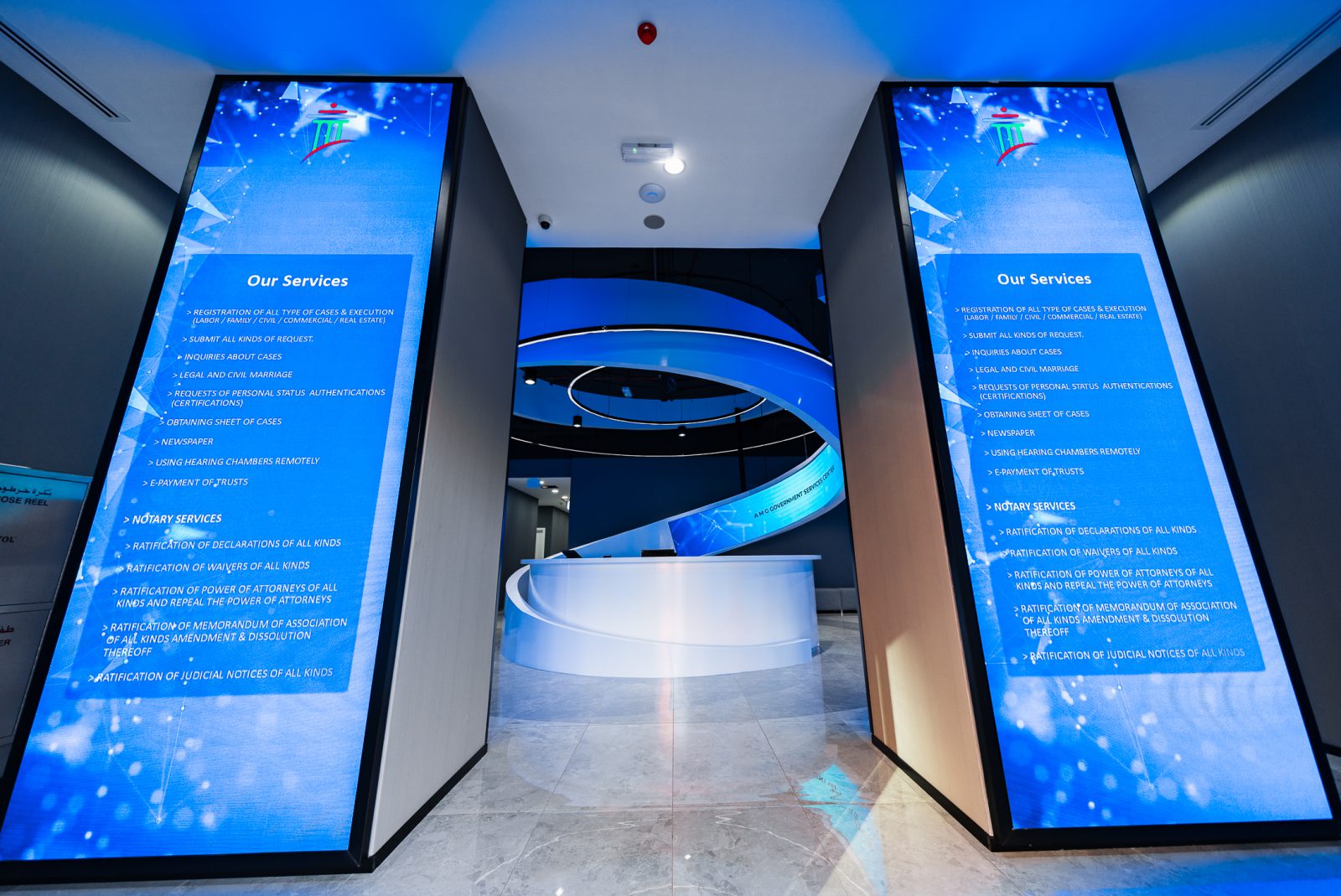 Main customer service hall of Al Adheed Center Dubai featuring ergonomic QMS counters, acoustic ceiling and Dubai Courts corporate branding