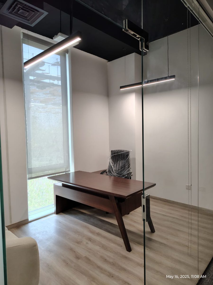 Frameless glass executive cabin with dark walnut executive desk, suspended LED lighting, and parquet flooring